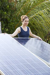 Lächelnde Frau steht hinter Sonnenkollektoren unter Palmen - NDF01420