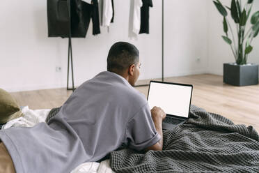 Junger Mann mit Laptop auf dem Bett liegend zu Hause - VPIF05686