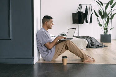 Smiling man using laptop sitting at home - VPIF05697