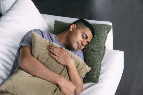 Young man with pillow sleeping on sofa in living room - VPIF05710