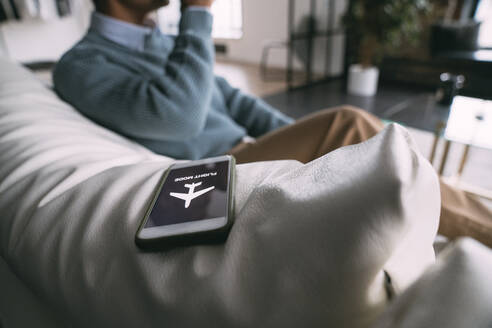 Flugzeugmodus-Symbol auf dem Mobiltelefon eines Mannes, der zu Hause auf dem Sofa sitzt - VPIF05736