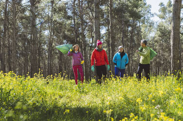 Freiwillige mit Müllsäcken bei einem Spaziergang im Wald an einem sonnigen Tag - JCCMF06056