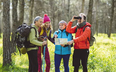 Mann schaut durch ein Fernglas, während Freunde im Wald eine Karte austauschen - JCCMF06068