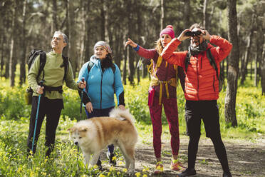 Mann schaut durch ein Fernglas und steht bei Freunden und Hund im Wald - JCCMF06075