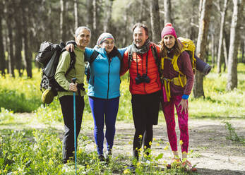 Lächelnde Freunde stehen zusammen im Wald an einem sonnigen Tag - JCCMF06076