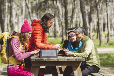 Reife Männer diskutieren über Tagebuch mit Frauen sitzen am Picknick-Tisch im Wald - JCCMF06080