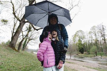Glücklicher Vater mit Töchtern unter Regenschirm stehend - TYF00119