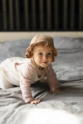 Smiling baby girl crawling on bed at home - SSGF00731