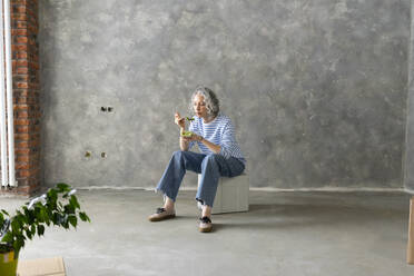 Woman eating lunch sitting on box in front of wall - SEAF00783