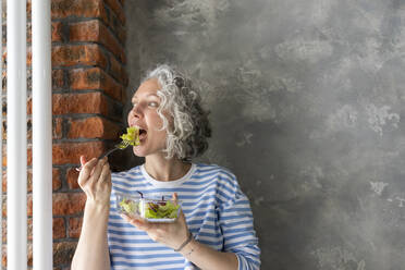 Frau isst frischen Salat zum Mittagessen vor einer grauen Wand - SEAF00785