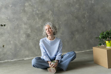 Woman with tea cup sitting on ground in front of wall - SEAF00796