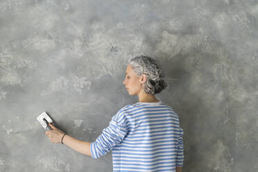 Woman with work tool working on gray wall - SEAF00802