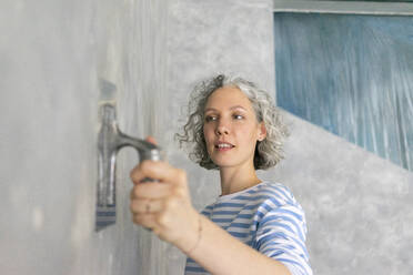 Frau bei der Arbeit an einer grauen Wand mit Arbeitswerkzeug - SEAF00803