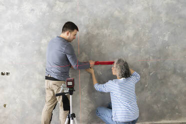 Woman and friend measuring construction laser level on gray wall - SEAF00812