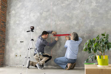 Woman and man measuring construction laser level on gray wall - SEAF00813