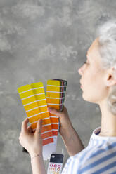 Frau wählt eine Farbe aus einer Farbpalette vor einer Wand aus - SEAF00824