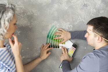 Woman and friend choosing color with swatch chart on gray wall - SEAF00825