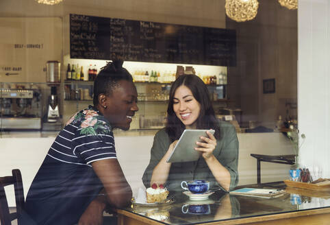 Lächelndes Paar, das in einem Café eine digitale Tafel betrachtet - ISF25612