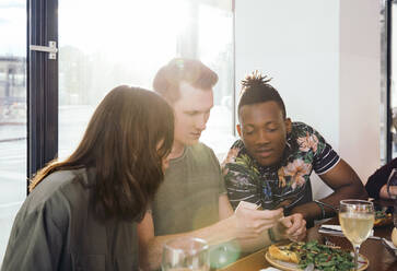 Freunde schauen im Restaurant auf ihr Smartphone - ISF25645