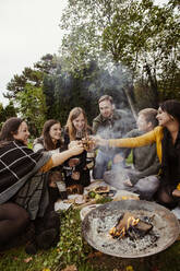 Group of friends toasting around fire pit in garden - ISF25667