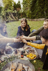 Eine Gruppe von Freunden stößt um eine Feuerstelle im Garten an - ISF25673