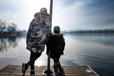 Italy, Rear view of brothers, on pier on calm lake - ISF25695