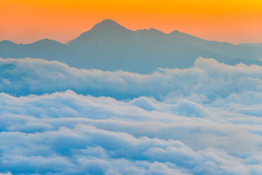 Atemberaubende Drohne Blick auf dicke weiße Wolken schweben gegen Berggipfel und orange Sonnenaufgang Himmel am Morgen in der Natur - ADSF34567