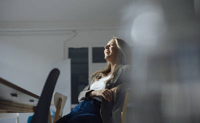 Happy businesswoman sitting on chair in conference room at office - JOSEF08481