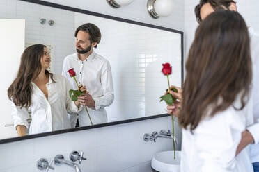Mann beschenkt Frau mit roter Rose vor einem Spiegel - DLTSF02904