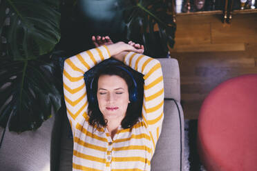 Woman wearing headphones relaxing on sofa at home - AMWF00258