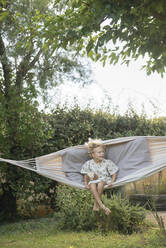 Playful girl swinging in hammock at garden - SVKF00116