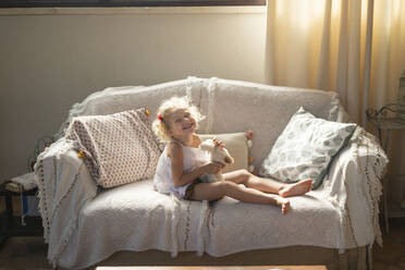 Glückliches Mädchen mit Spielzeug auf dem Sofa zu Hause - SVKF00127