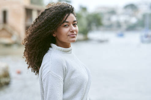 Young woman with curly hair in front of sea - KIJF04427