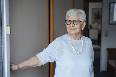 Glückliche ältere Frau mit weißem Haar steht an der Tür - JOSEF08525