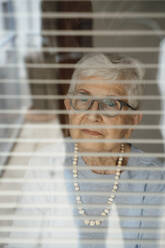 Retired senior woman seen through window blinds - JOSEF08582