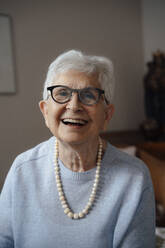 Happy senior woman wearing eyeglasses sitting at home - JOSEF08590