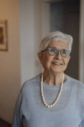 Smiling senior woman wearing eyeglasses standing at home - JOSEF08594