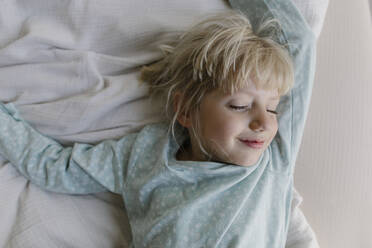 Smiling girl with eyes closed lying on bed at home - TYF00122