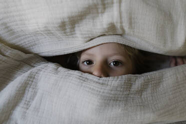 Girl peeking out from blanket at home - TYF00126