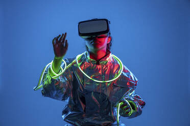 Frau in virtueller Realität hält Neonlicht vor blauem Hintergrund - VPIF05780