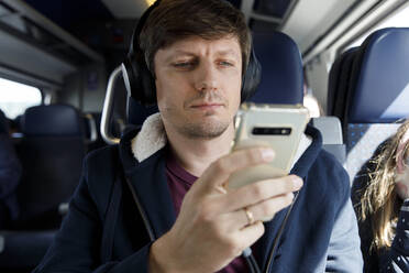 Man wearing wireless headphones using mobile phone in train - TYF00128