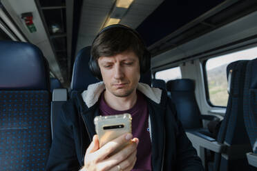 Man with headphones using smart phone sitting on seat in train - TYF00129