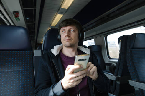 Mann mit Mobiltelefon hört Musik über Kopfhörer im Zug - TYF00130