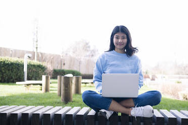 Lächelnde junge Frau mit Laptop auf dem Sitz sitzend - AMWF00274
