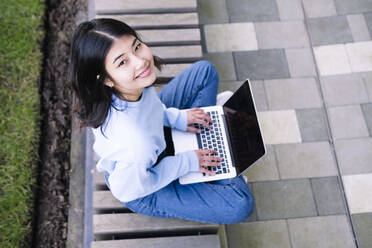 Happy young woman sitting on seat with laptop - AMWF00275