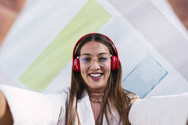 Glückliche Frau mit drahtlosen Kopfhörern vor einer Wand - PNAF03670