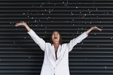 Happy young woman throwing confetti in front of corrugated iron shutter - PNAF03700