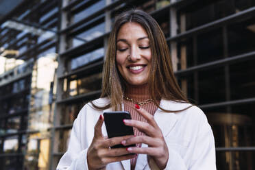 Happy businesswoman using smart phone at office building - PNAF03710