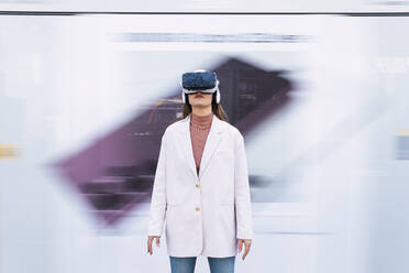 Geschäftsfrau mit Virtual-Reality-Simulator vor einer Wand stehend - PNAF03715