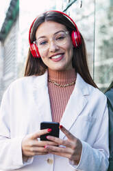 Lächelnde junge Frau mit Kopfhörern und Smartphone - PNAF03729